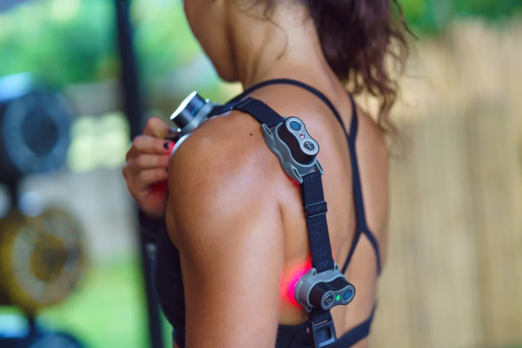 woman wears a Kineon red light therapy device on her shoulder