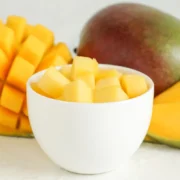 a cup of diced mango next to a whole mango