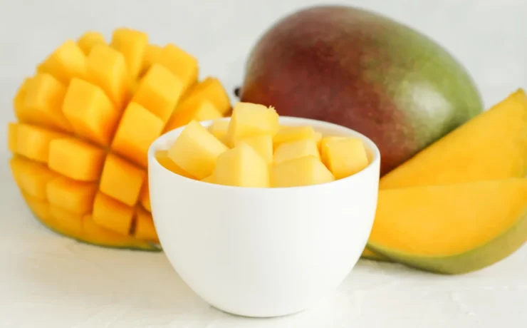 a cup of diced mango next to a whole mango