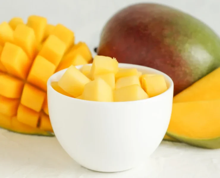 a cup of diced mango next to a whole mango