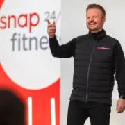 a man on stage wearing a Snap Fitness vest in front of a Snap Fitness sign.