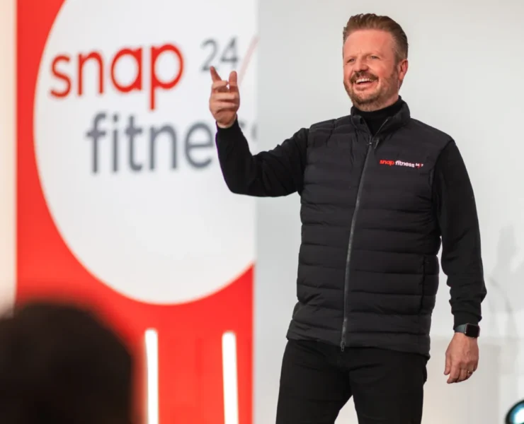 a man on stage wearing a Snap Fitness vest in front of a Snap Fitness sign.